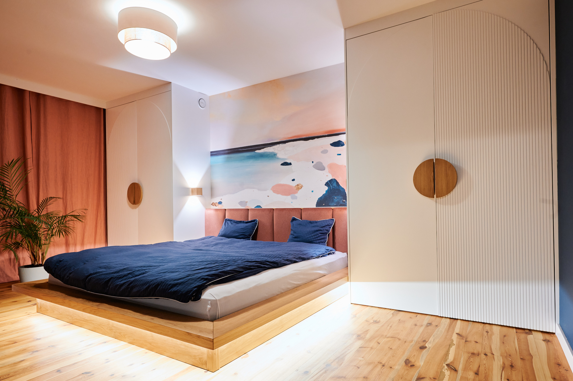 Nowoczesna jadalnia z drewnianym stołem, kolorowymi krzesłami, zdjęciami na ściaSypialnia z dużym niskim ł&oacute;żkiem, pastelowym muralem, zabudową meblową z dekoracyjnymi uchwytami.